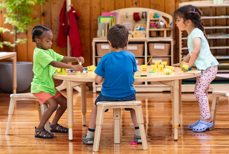 Three children sitting on stools and working around a table