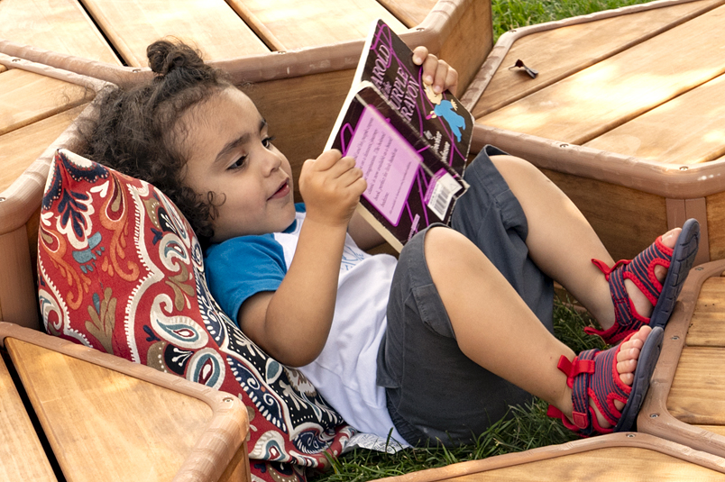 A child on a pillow reading a book outside