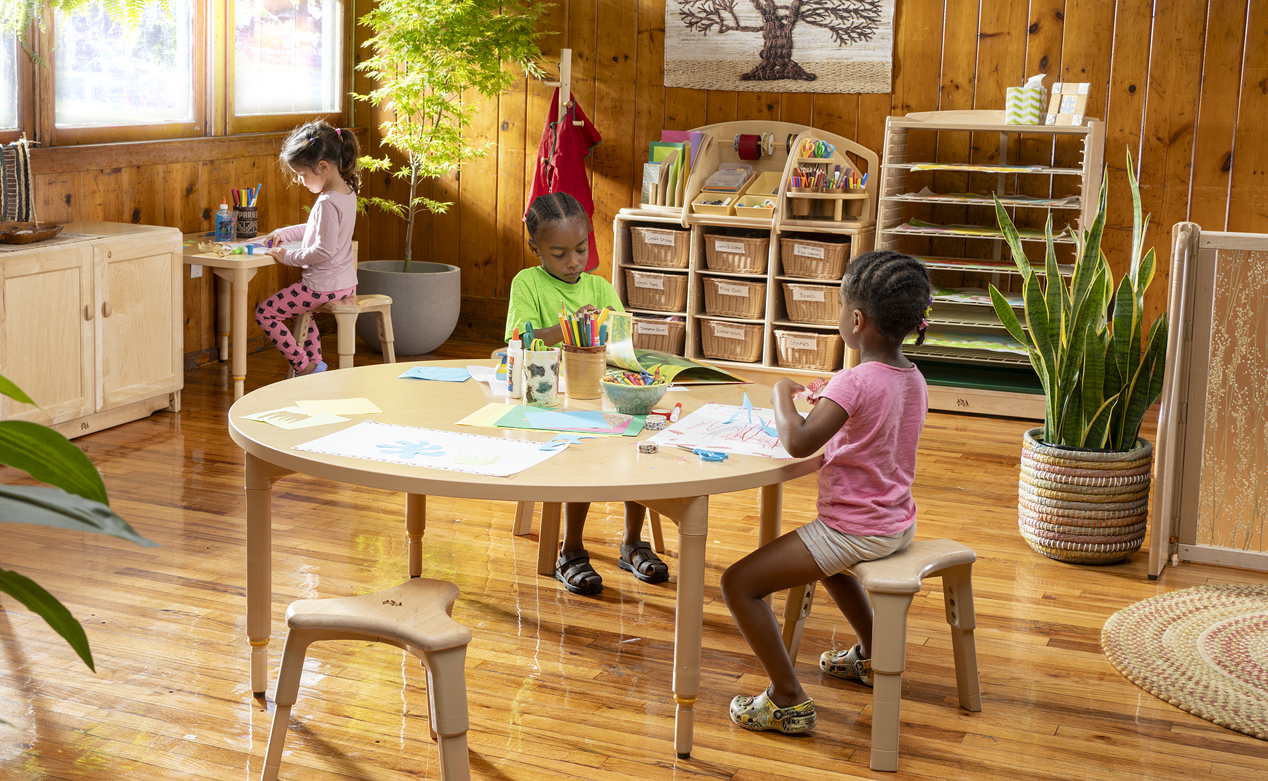 Two children doing arts and crafts at a table, with another child writing at a table