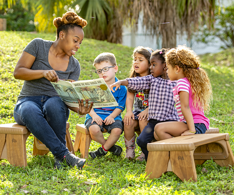 A teacher reading a book to kids outside